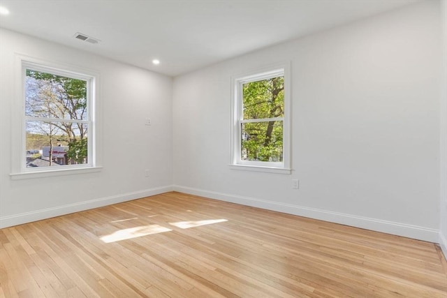 empty room with baseboards, visible vents, a healthy amount of sunlight, and light wood finished floors