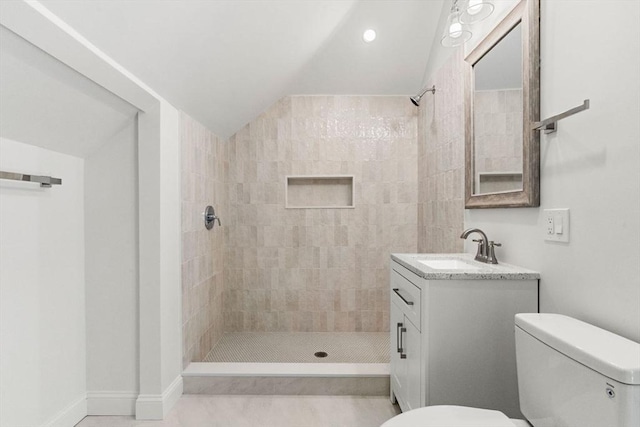 bathroom with toilet, tiled shower, lofted ceiling, and vanity