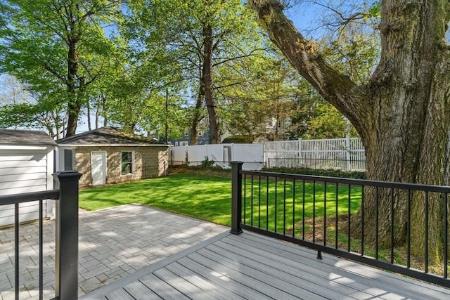 wooden deck featuring a lawn, a patio, an outdoor structure, and a fenced backyard