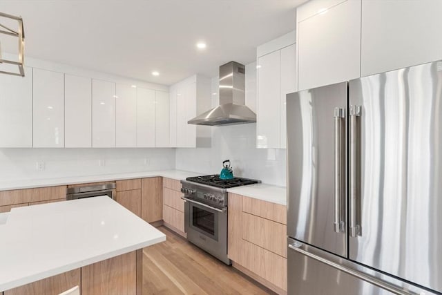 kitchen with wall chimney range hood, high end appliances, decorative backsplash, and modern cabinets