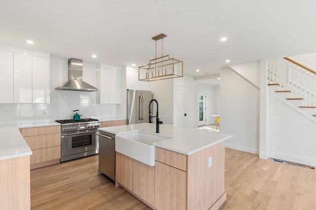 kitchen featuring wall chimney range hood, high end appliances, modern cabinets, light wood-type flooring, and a sink