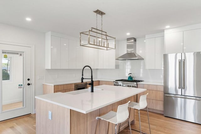 kitchen with wall chimney range hood, appliances with stainless steel finishes, modern cabinets, tasteful backsplash, and light wood finished floors