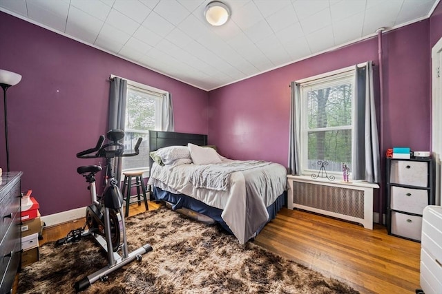 bedroom with wood finished floors, crown molding, and radiator heating unit