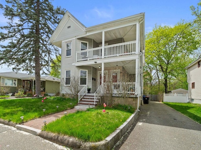 view of front facade featuring covered porch, fence, a balcony, and a front yard