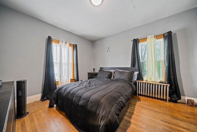 bedroom with radiator heating unit, baseboards, and light wood finished floors