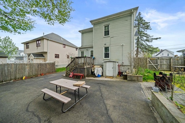rear view of house with a wooden deck, a patio area, an outdoor structure, a fenced backyard, and a storage unit