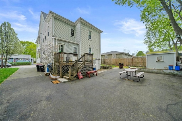 rear view of house featuring an outdoor structure, fence, a deck, a patio area, and a storage shed