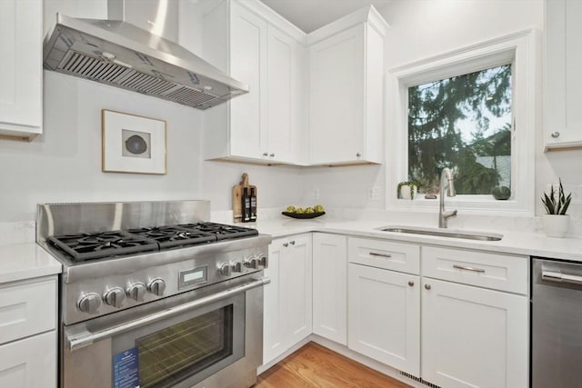 kitchen with sink, light wood-type flooring, white cabinetry, wall chimney range hood, and stainless steel appliances