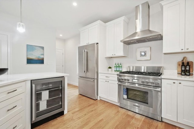 kitchen featuring pendant lighting, premium appliances, white cabinetry, wall chimney range hood, and wine cooler