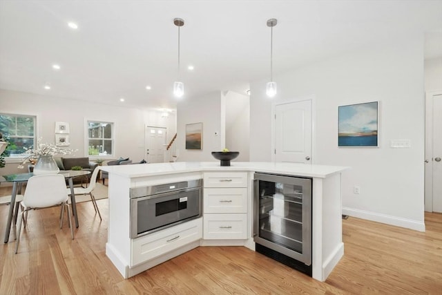 kitchen with light hardwood / wood-style flooring, wine cooler, decorative light fixtures, white cabinets, and a center island