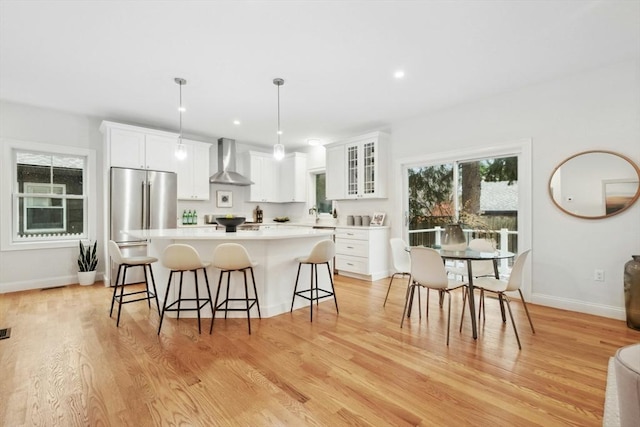 kitchen with pendant lighting, light hardwood / wood-style flooring, white cabinetry, wall chimney range hood, and high end refrigerator