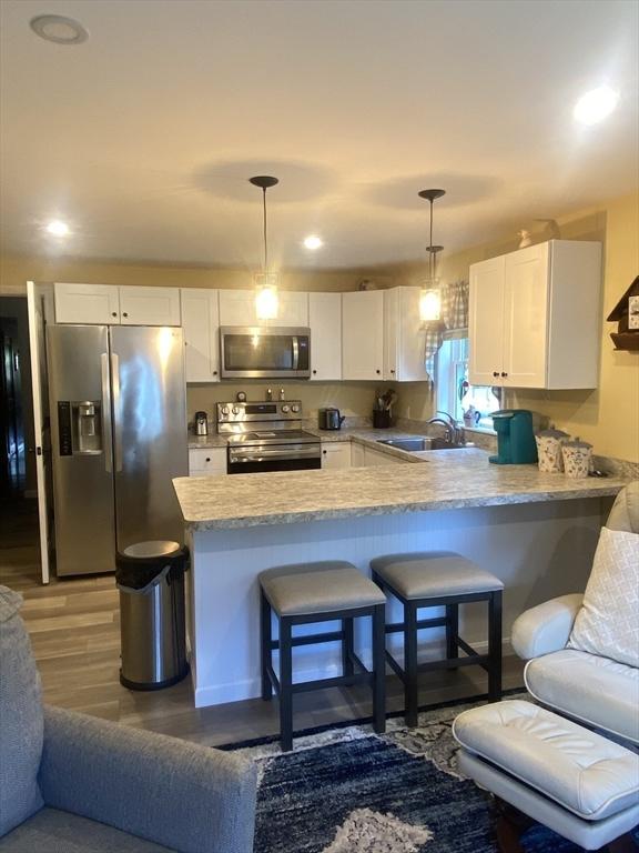 9 Pine City Rd, Carver, MA 02330 - kitchen with stainless steel appliances, a sink, a peninsula, white cabinets, and light wood-type flooring