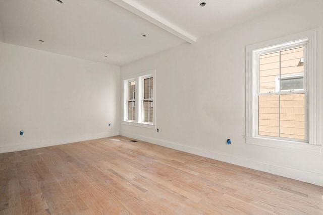 empty room featuring beamed ceiling, light wood finished floors, and baseboards