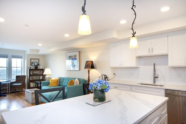 kitchen with stainless steel dishwasher, white cabinetry, sink, and hanging light fixtures