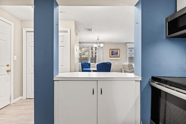 kitchen featuring a notable chandelier, electric range oven, white cabinets, and light hardwood / wood-style flooring