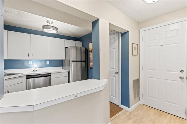 kitchen featuring sink, appliances with stainless steel finishes, white cabinets, kitchen peninsula, and light wood-type flooring