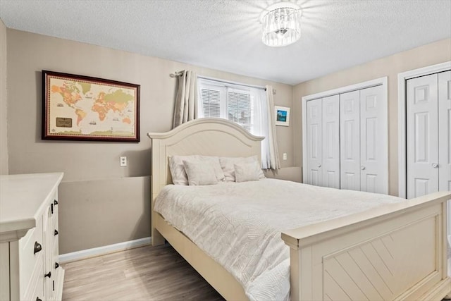 bedroom featuring two closets, a textured ceiling, and light wood-type flooring