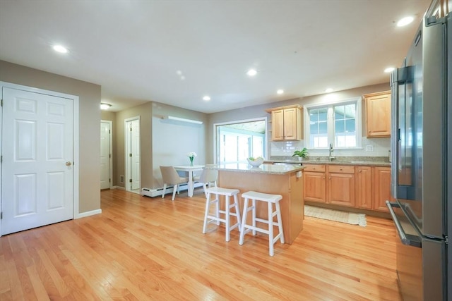 kitchen featuring stainless steel fridge, a center island, light wood-type flooring, and a kitchen bar