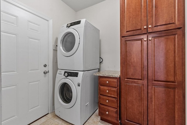 laundry area featuring cabinets, stacked washing maching and dryer, and light tile patterned flooring