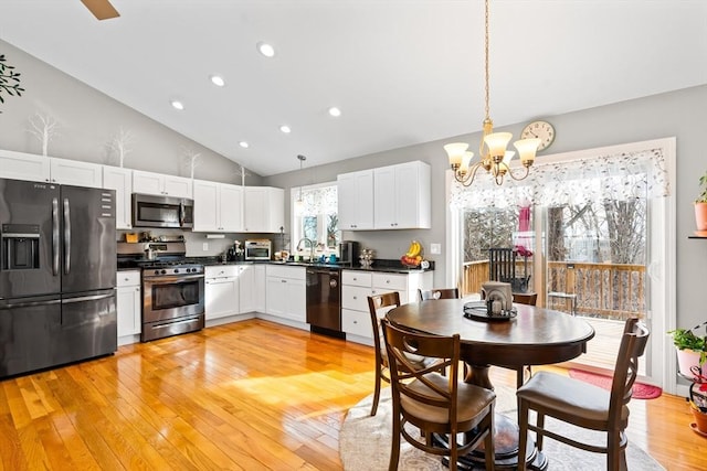 kitchen featuring pendant lighting, light wood finished floors, dark countertops, white cabinetry, and black appliances