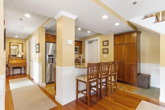 kitchen featuring light wood-type flooring, a peninsula, appliances with stainless steel finishes, and brown cabinetry