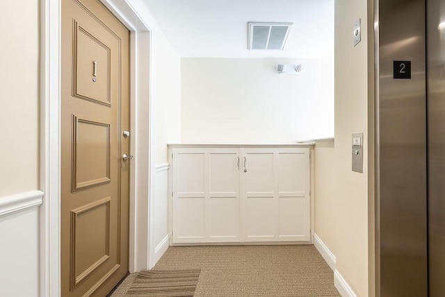 hallway featuring elevator, visible vents, light carpet, and baseboards