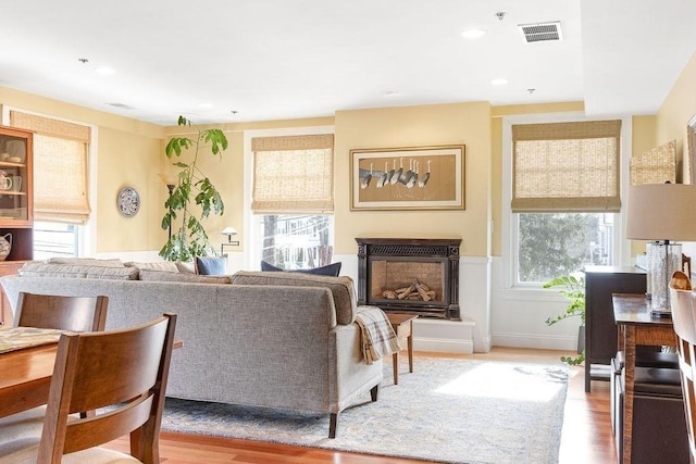 living area featuring light wood finished floors, recessed lighting, visible vents, and a glass covered fireplace