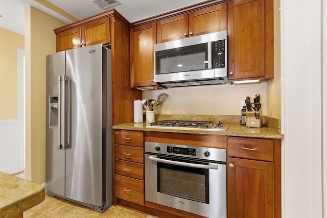 kitchen featuring stainless steel appliances, light stone countertops, visible vents, and brown cabinets