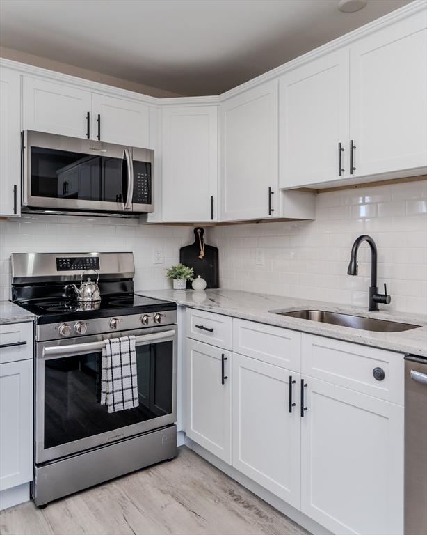 kitchen with white cabinets, appliances with stainless steel finishes, light wood-type flooring, and sink