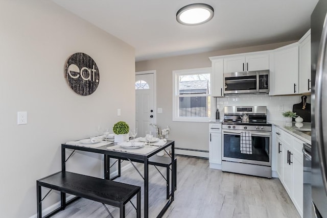 kitchen with backsplash, stainless steel appliances, baseboard heating, light hardwood / wood-style flooring, and white cabinets