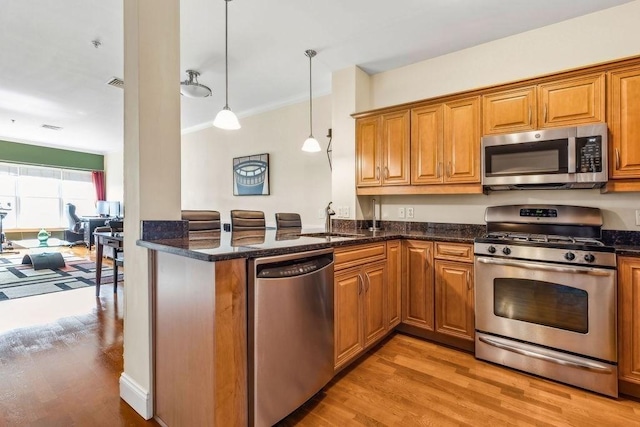 kitchen featuring appliances with stainless steel finishes, light wood-type flooring, a sink, brown cabinetry, and ornamental molding