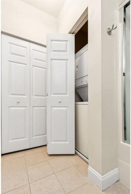 clothes washing area with stacked washer and clothes dryer and light tile patterned floors