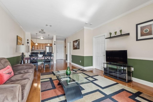 living area with wood finished floors, ornamental molding, and baseboards