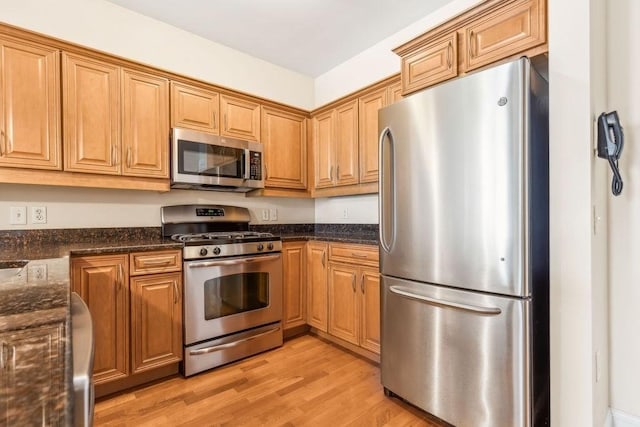 kitchen featuring appliances with stainless steel finishes, light wood-style flooring, dark stone countertops, and brown cabinetry