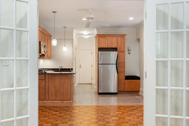 kitchen with stainless steel appliances, dark countertops, brown cabinetry, a ceiling fan, and decorative backsplash