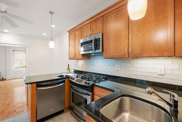 kitchen with stainless steel appliances, a sink, brown cabinetry, crown molding, and a ceiling fan