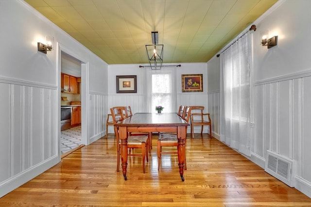 108 Needham St, Dedham, MA 02026 - dining room featuring ornamental molding, light wood-type flooring, a wainscoted wall, and a decorative wall
