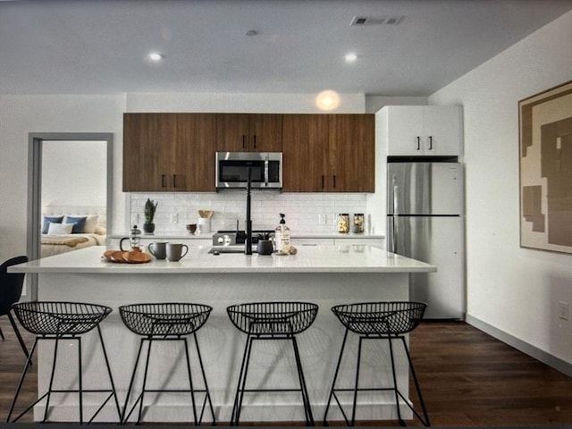 kitchen with decorative backsplash, a kitchen island with sink, a kitchen bar, light countertops, and stainless steel appliances