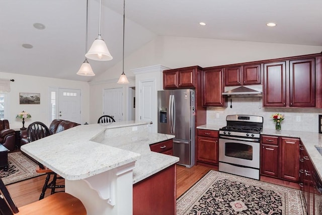 kitchen featuring reddish brown cabinets, a breakfast bar, a center island, stainless steel appliances, and under cabinet range hood