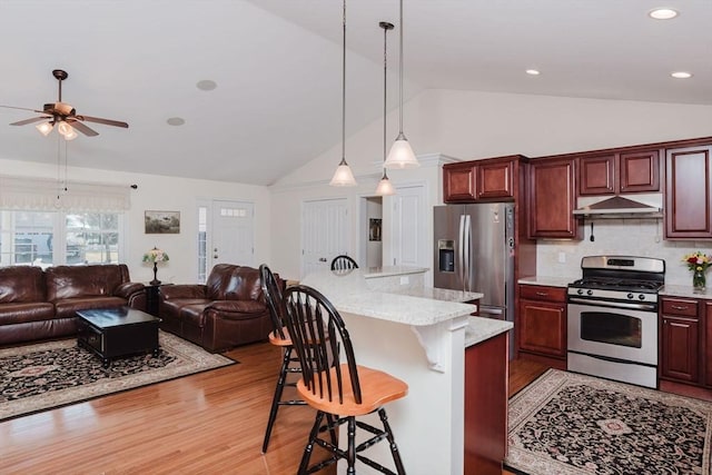 kitchen featuring open floor plan, appliances with stainless steel finishes, a kitchen breakfast bar, and under cabinet range hood