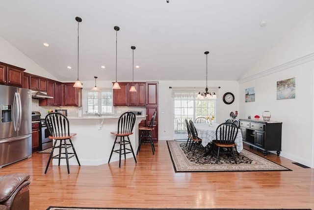 kitchen with light wood-style floors, appliances with stainless steel finishes, a breakfast bar, hanging light fixtures, and under cabinet range hood