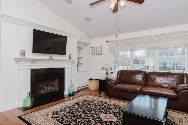 living area featuring built in features, lofted ceiling, a fireplace with flush hearth, ceiling fan, and wood finished floors