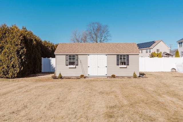 view of front of house with a shingled roof, an outdoor structure, a front lawn, and fence