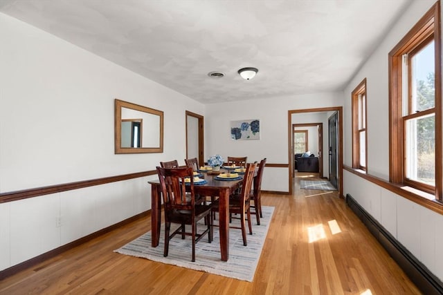 5 Crescent Ln, Sudbury, MA 01776 - dining room with visible vents, light wood-style flooring, a baseboard heating unit, and a wainscoted wall