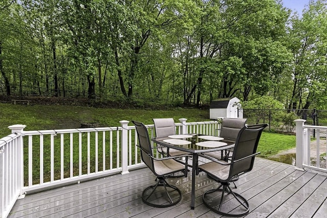 wooden deck featuring outdoor dining area, a storage unit, and an outbuilding