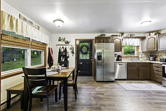 kitchen with appliances with stainless steel finishes, a baseboard heating unit, wood finished floors, light countertops, and dark brown cabinets
