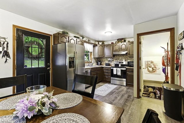 kitchen with stainless steel appliances, under cabinet range hood, light wood-style floors, light countertops, and backsplash