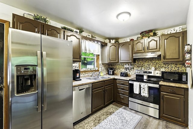 kitchen featuring appliances with stainless steel finishes, under cabinet range hood, a sink, dark brown cabinets, and light wood-type flooring