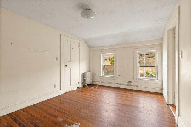 unfurnished room with radiator, hardwood / wood-style floors, and vaulted ceiling