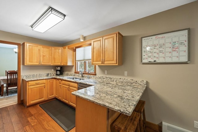 kitchen featuring sink, wood-type flooring, light stone countertops, light brown cabinetry, and kitchen peninsula